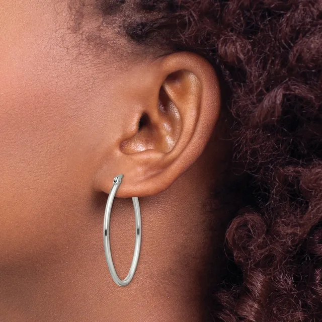 A person wearing a pair of silver hoop earrings, shown from the side profile with their ear and dark curly hair visible.