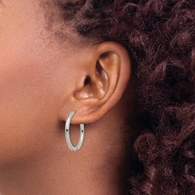 A person with textured dark hair wearing a polished silver-toned oval hoop earring in their earlobe, shown in profile view.