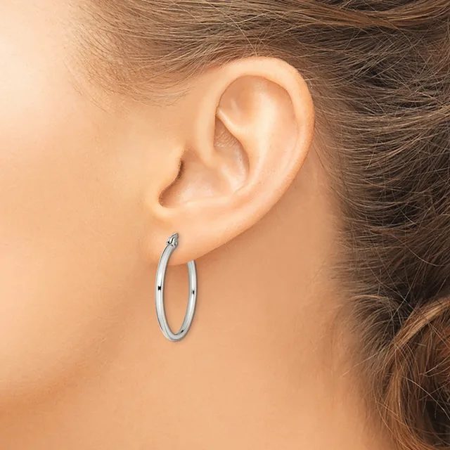 A person wearing a polished silver hoop earring in their pierced earlobe, shown in profile view.
