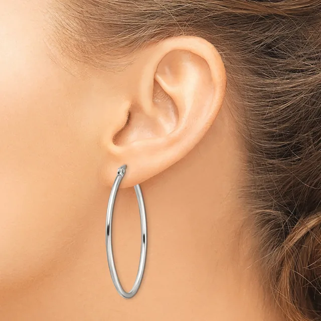 A woman wearing a pair of polished silver hoop earrings, shown from the side profile of her ear and neck.