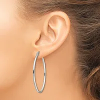 A woman wearing a pair of polished silver hoop earrings, shown from the side profile of her ear and neck.