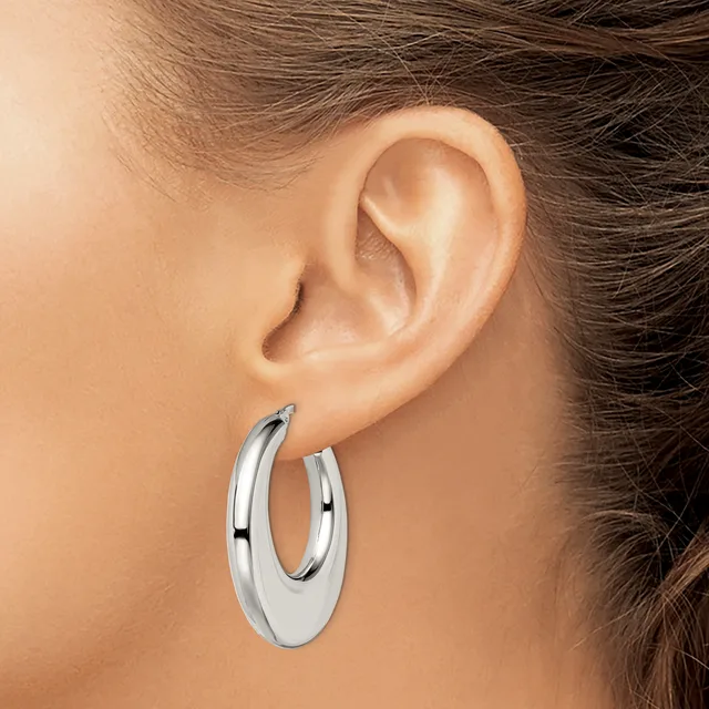 A woman wearing polished silver hoop earrings, shown in profile with her ear and side of her face visible.