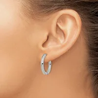 A pair of polished silver hoop earrings worn on a person's earlobes, shown in profile against bare skin.
