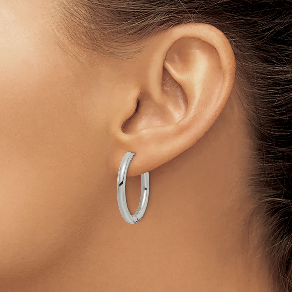 A woman wearing a pair of polished silver hoop earrings, shown from the side profile of her face and ear.