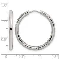 A pair of polished silver-toned hoop earrings displayed next to a ruler showing their dimensions of approximately 1.25 inches in diameter.