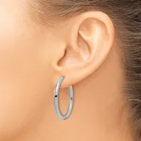 A person wearing a pair of polished silver-toned hoop earrings, shown from the side view of their ear and head.
