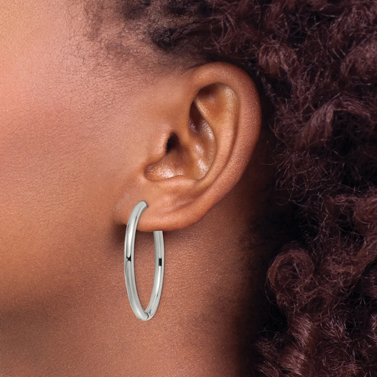 A person wearing a pair of polished silver hoop earrings, shown in profile with dark curly hair pulled back.