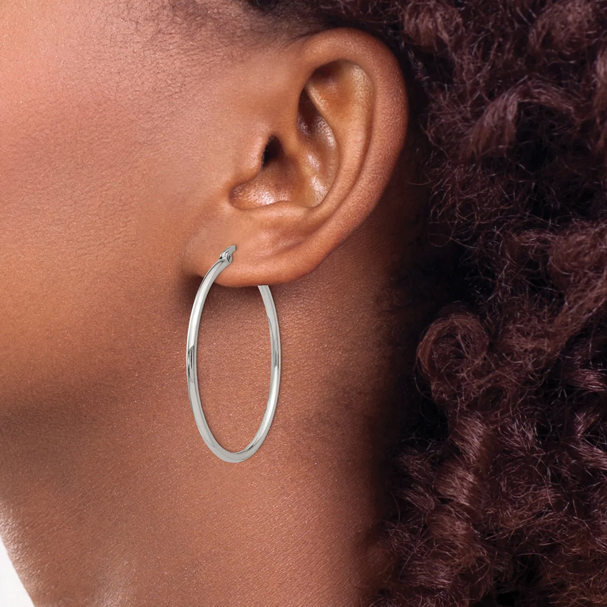 A person wearing a large oval silver hoop earring in their earlobe, shown in profile against their shoulder and curly dark hair.