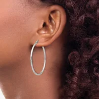 A person wearing a large oval silver hoop earring in their earlobe, shown in profile against their shoulder and curly dark hair.