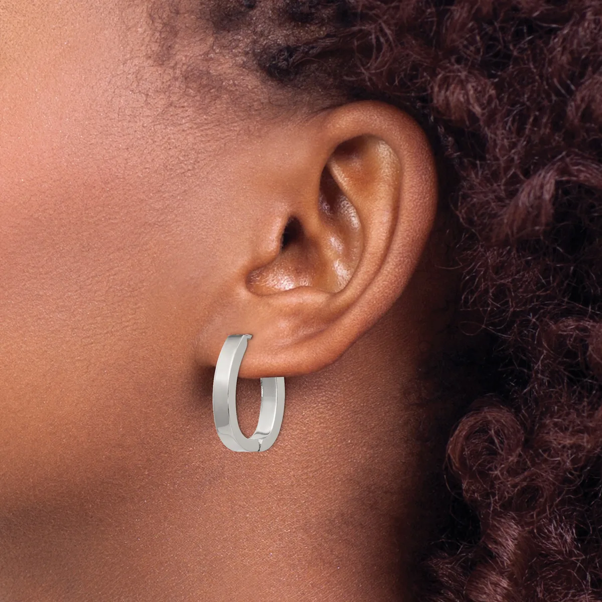 A person wearing a pair of polished silver-toned chunky hoop earrings, shown from the side profile of their face and ear.