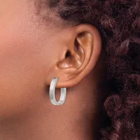 A person wearing a pair of polished silver-toned chunky hoop earrings, shown from the side profile of their face and ear.