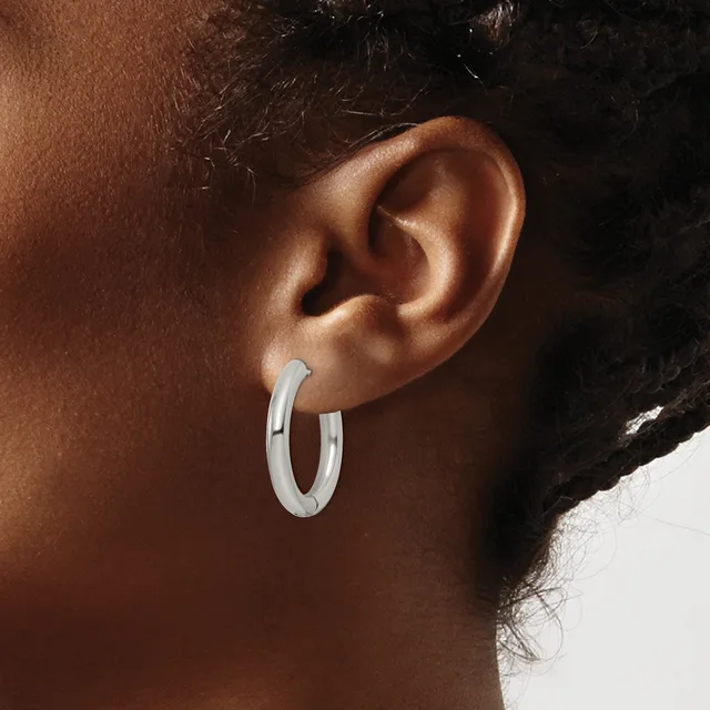 A person wearing a pair of polished silver hoop earrings, shown from the side profile of their ear and neck.