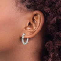 A person wearing a silver hoop earring in their earlobe, shown in profile against their ear and dark curly hair.