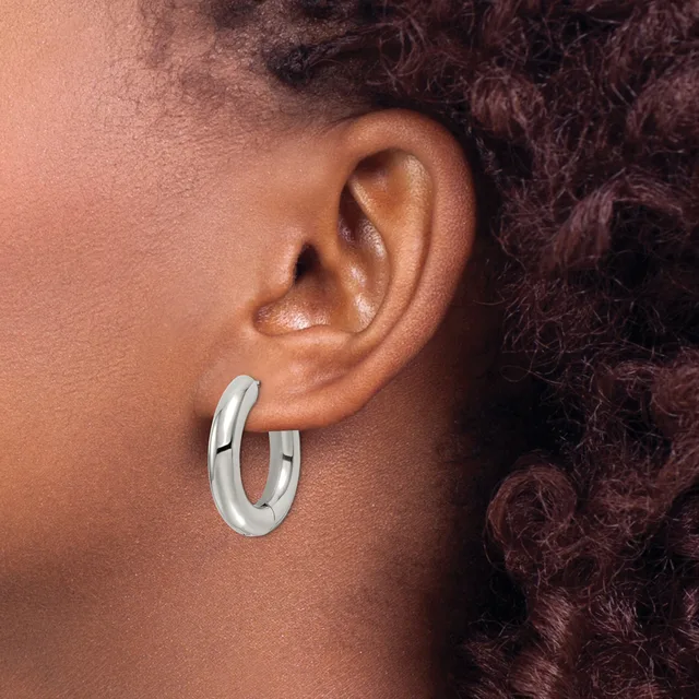 A person wearing polished silver-toned hoop earrings, shown from the side with dark curly hair visible in the background.