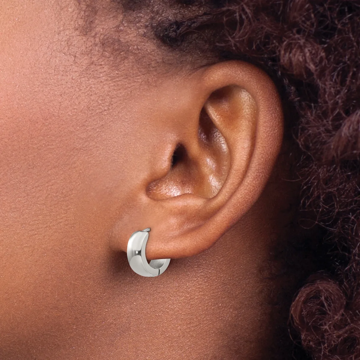 A person wearing a polished silver curved hoop earring in their earlobe, shown in profile against their neck and shoulder.