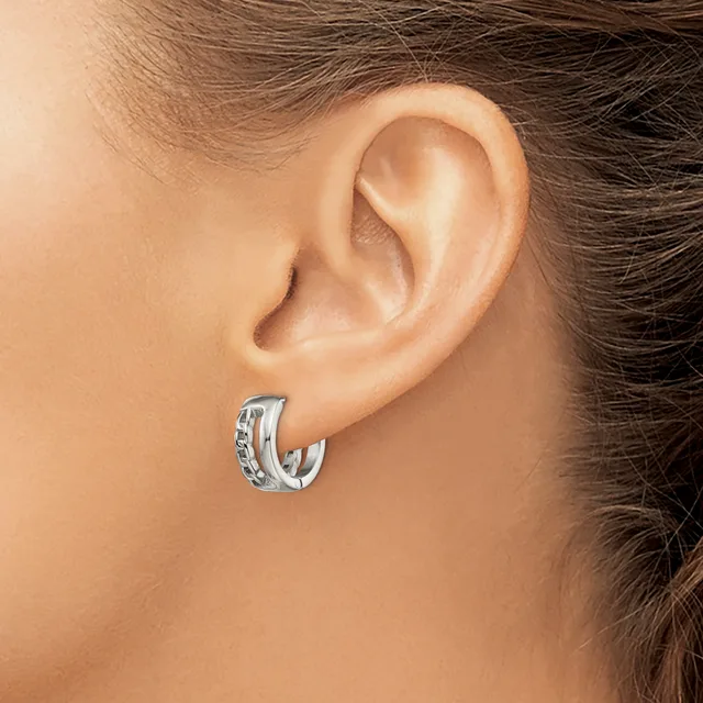 A silver hoop earring with a textured surface worn on a person's earlobe.
