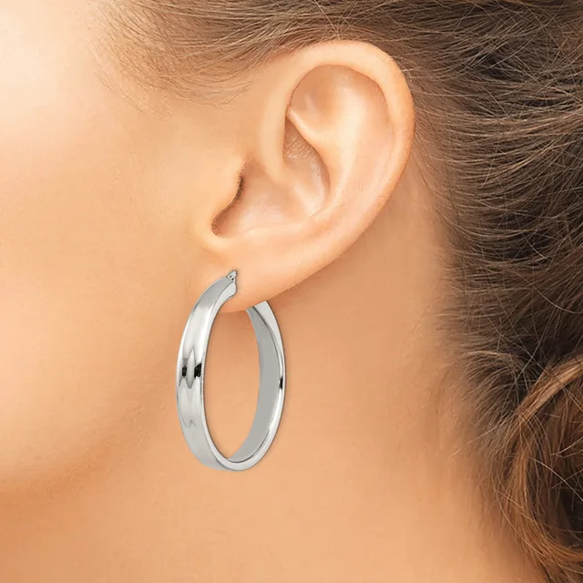 A woman wearing polished silver hoop earrings with a curved, tubular design, shown from the side profile view.