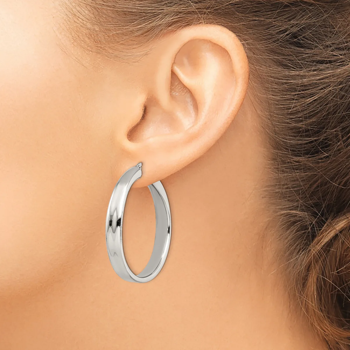A woman wearing polished silver hoop earrings with a curved, tubular design, shown from the side profile view.