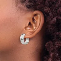 A polished silver curved hoop earring worn on the earlobe of a person with medium-toned skin and dark curly hair.