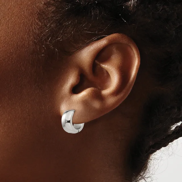 A polished silver chunky curved hoop earring worn on the earlobe of a person with medium brown skin tone and dark hair.