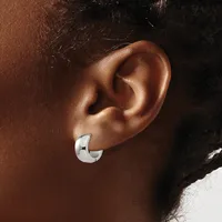 A polished silver chunky curved hoop earring worn on the earlobe of a person with medium brown skin tone and dark hair.