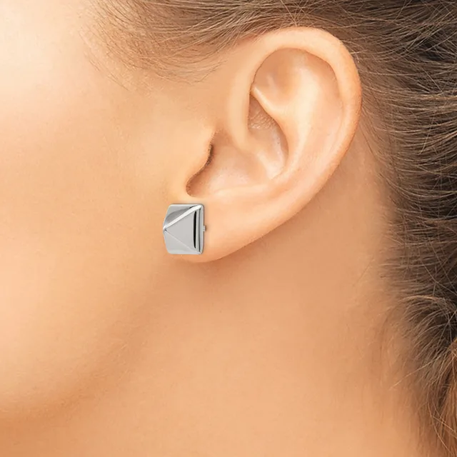 A silver rectangular stud earring with diagonal line detailing worn on a person's earlobe.