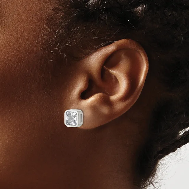 A silver square stud earring with a rectangular white gemstone sits on a person's earlobe.