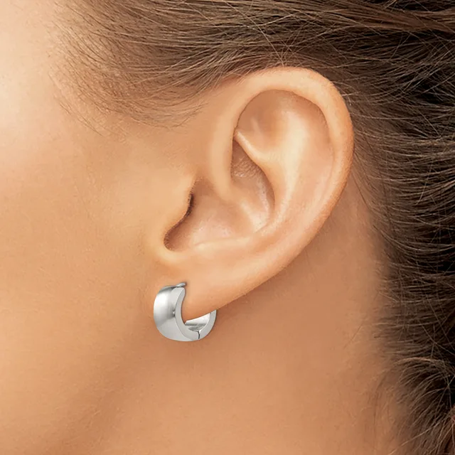 A polished silver curved hoop earring worn on the earlobe of a person with brown hair.