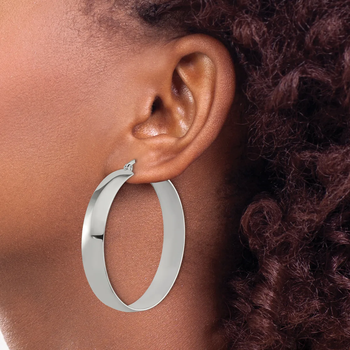 A person wearing a large polished silver hoop earring on their earlobe, shown in profile view against their shoulder and dark curled hair.