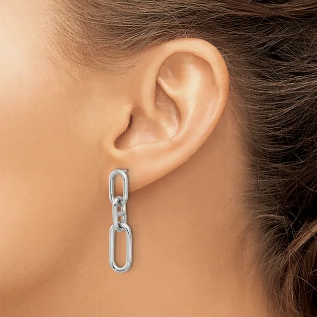 A person wearing a pair of silver chain link drop earrings hanging from pierced earlobes.