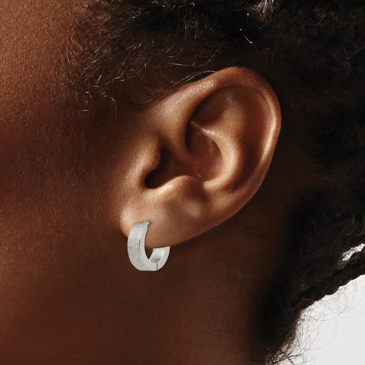 A silver curved hoop earring worn on the earlobe of a person with brown skin and dark hair.