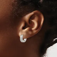 A silver curved hoop earring worn on the earlobe of a person with brown skin and dark hair.