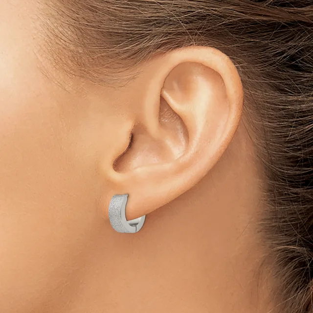 A person wearing a curved silver hoop earring in their earlobe, shown from the side profile of their head and ear.