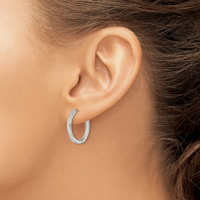 A woman wearing small silver textured hoop earrings, shown from the side profile of her head and ear.