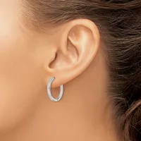 A woman wearing small silver textured hoop earrings, shown from the side profile of her head and ear.