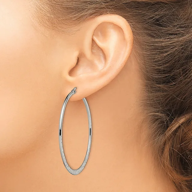 A woman wearing large oval hoop earrings with a textured surface, shown from the side profile of her face and ear.