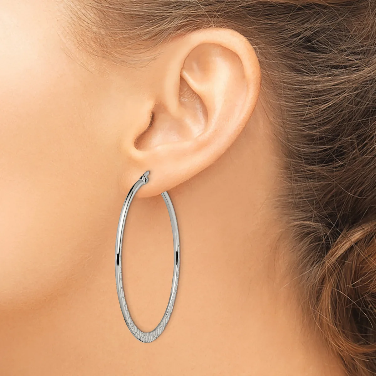 A woman wearing large oval hoop earrings with a textured surface, shown from the side profile of her face and ear.