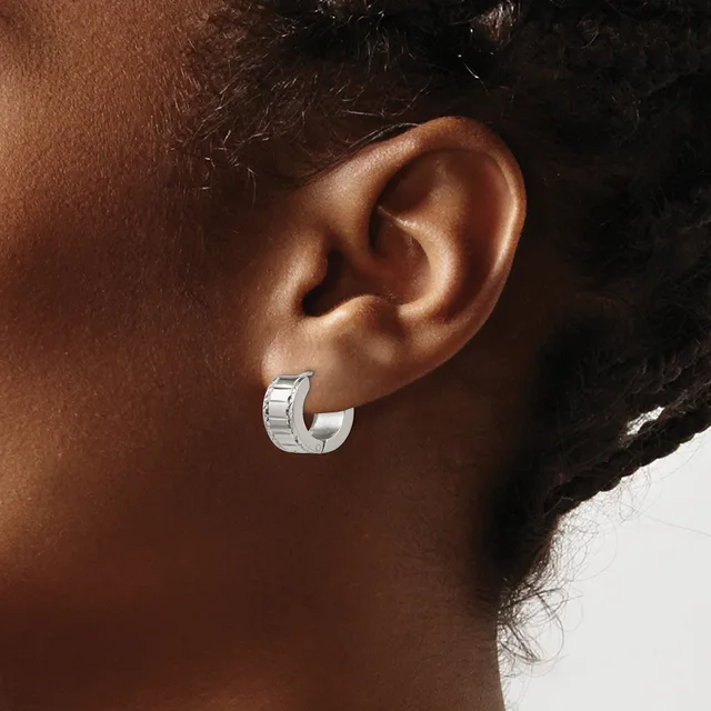 A close-up view of a person's ear wearing a small silver hoop earring with a textured, grooved surface.