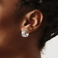 A close-up view of a person's ear wearing a small silver hoop earring with a textured, grooved surface.