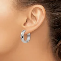 A woman wearing polished silver hoop earrings with a textured diamond-cut pattern on the outer surface, shown from the side profile.