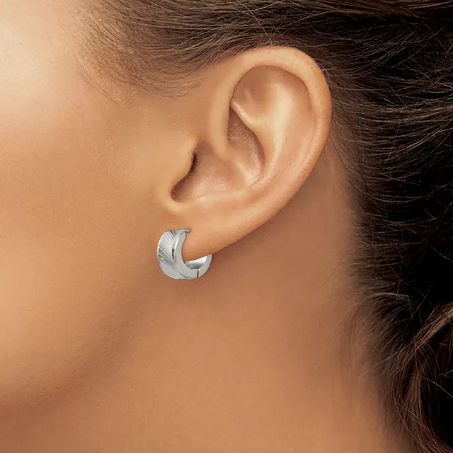 A person wearing a curved crescent-shaped silver earring with a textured surface in their pierced earlobe.