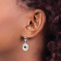 A person wearing a pair of silver drop earrings with circular pendants featuring black center stones surrounded by textured metalwork.