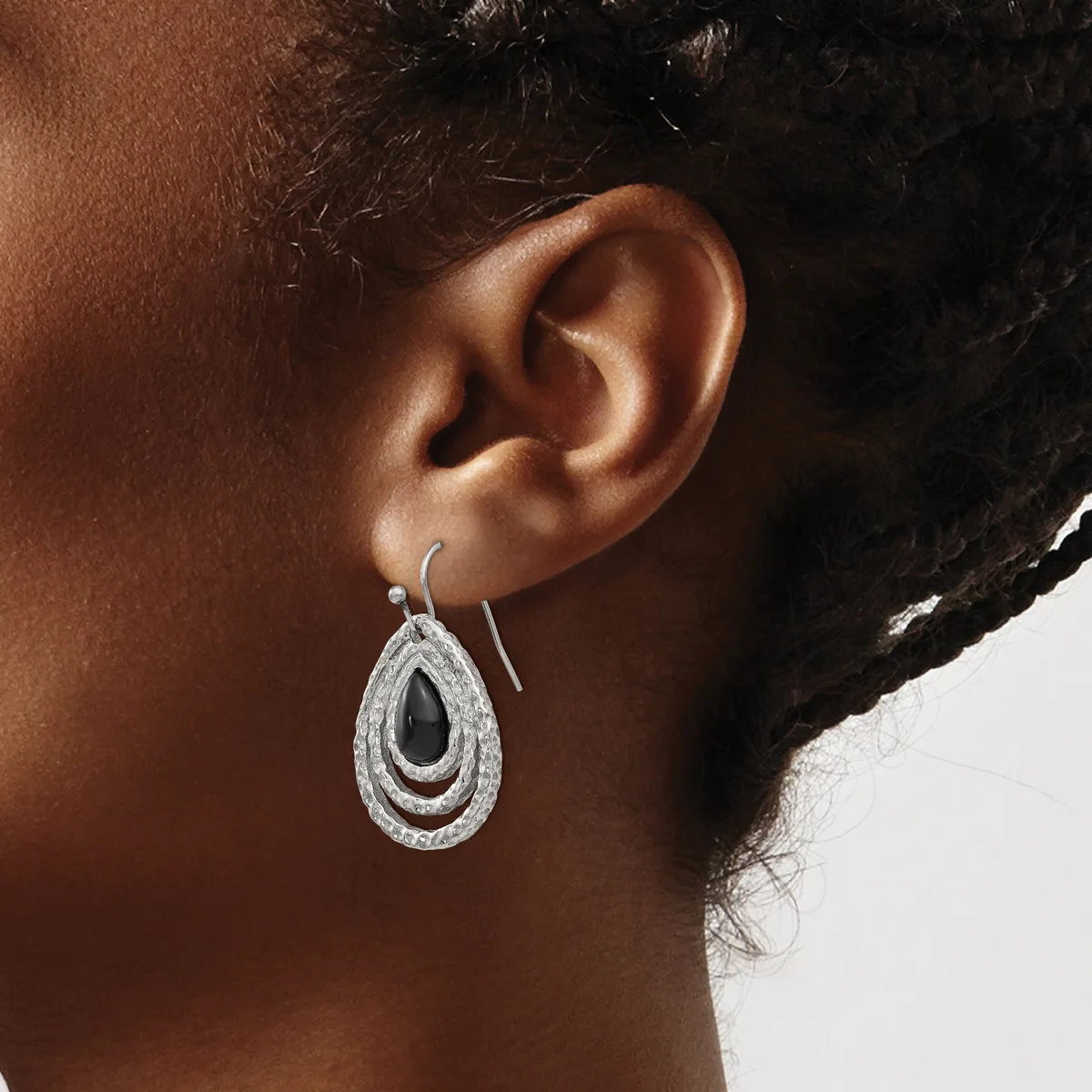 A person wearing a teardrop-shaped silver earring with a black stone center and textured concentric oval bands, shown from the side view of their ear.