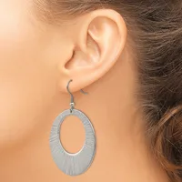 A woman wearing a silver-toned oval dangle earring with a textured brushed finish, shown from the side view of her ear.