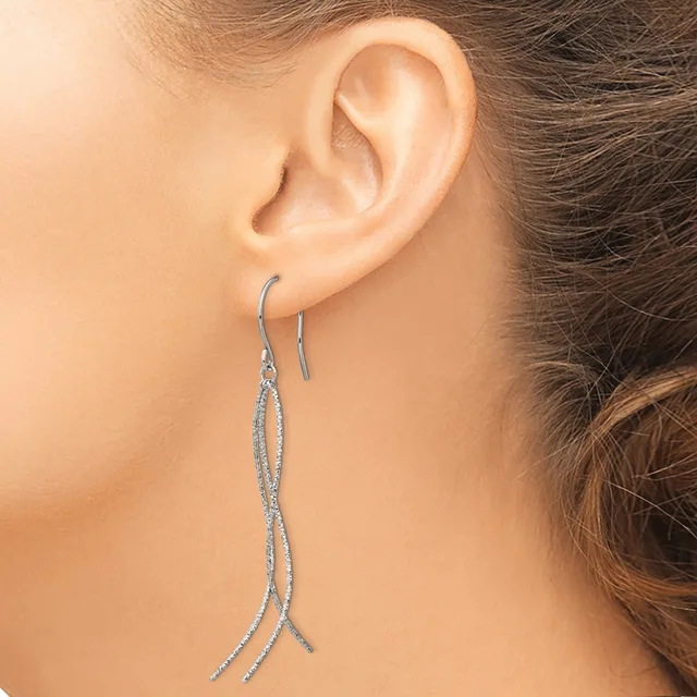 A person wearing long, thin silver-colored threader earrings that dangle past the earlobe, shown from the side view of their ear and neck.