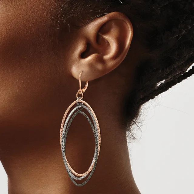 A person wearing rose gold and diamond oval hoop earrings with nested concentric ovals, shown from the side against their neck and shoulder.