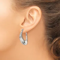 A woman wearing a pair of silver hoop earrings with a textured, hammered finish on her ears.
