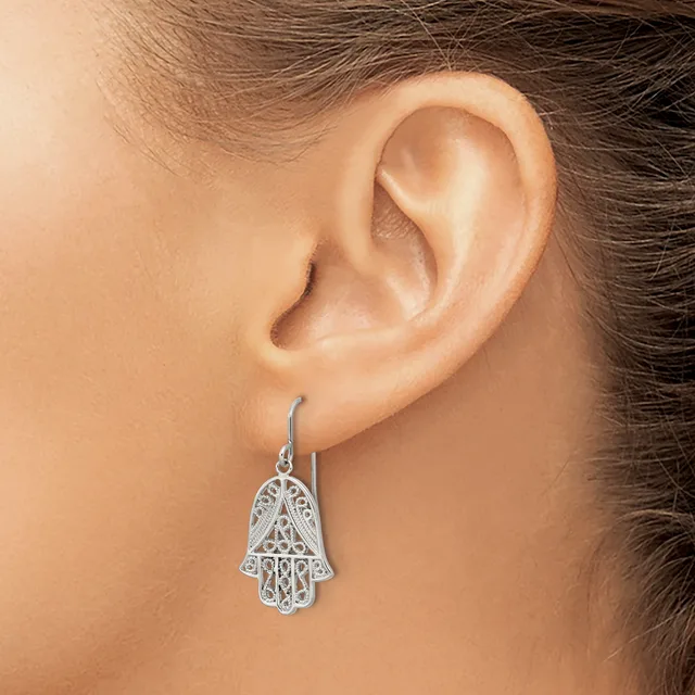 A silver filigree hamsa hand earring with intricate cutout details hangs from a hook through a pierced earlobe.
