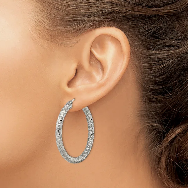A person wearing textured silver hoop earrings with a hammered or dimpled surface finish, shown from the side profile of their ear.