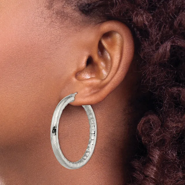 A person wearing a textured silver hoop earring, shown in profile against their ear and shoulder with dark curly hair visible in the background.